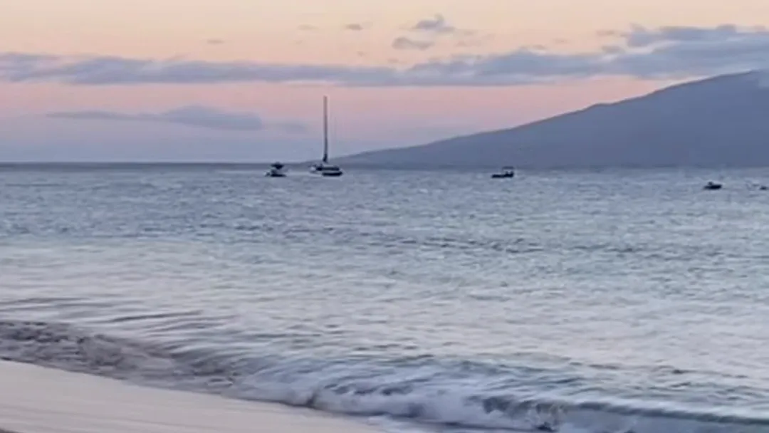 Dawn over a quiet bay: a sailboat at anchor, a mountain ridge across the water, and the sky turning pink before sunrise