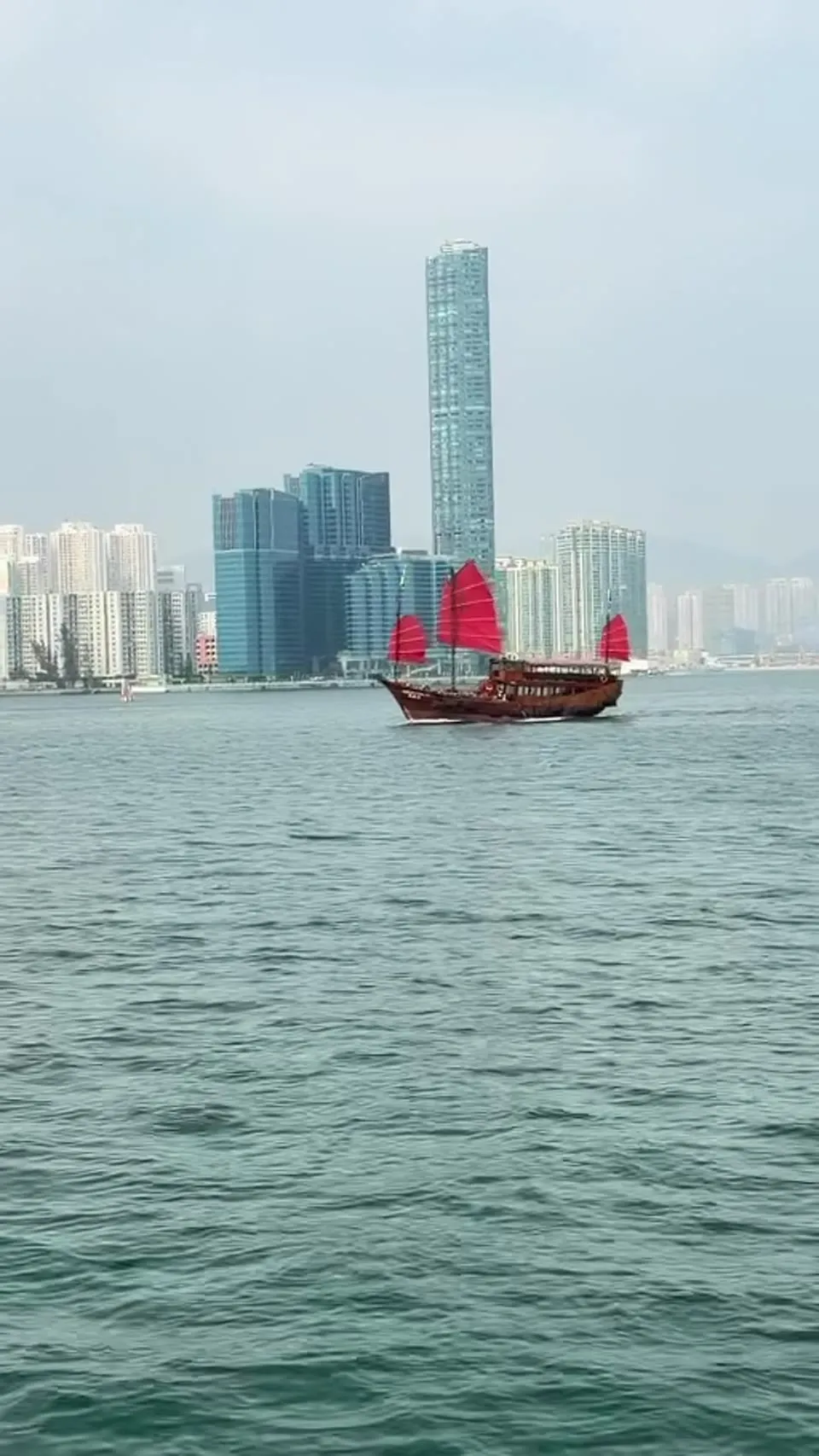 A red-sail junk on Victoria Harbour with the skyline behind it