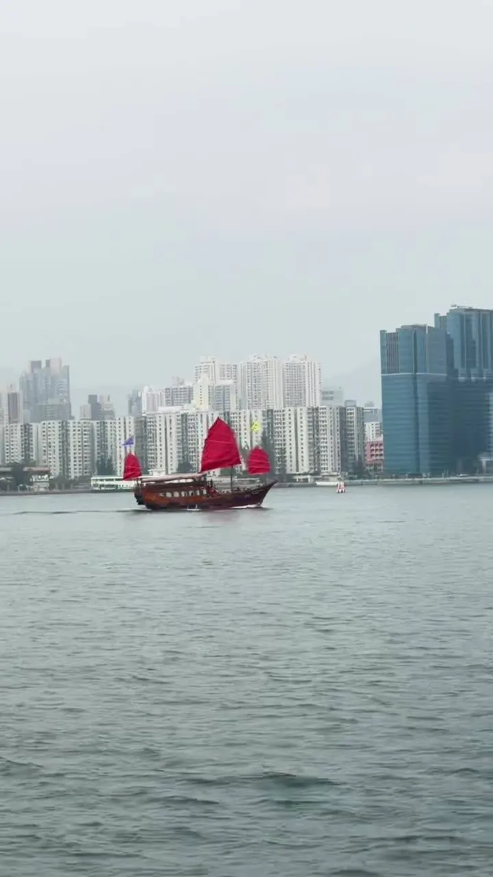 Red-sail junk crossing Victoria Harbour with towers behind