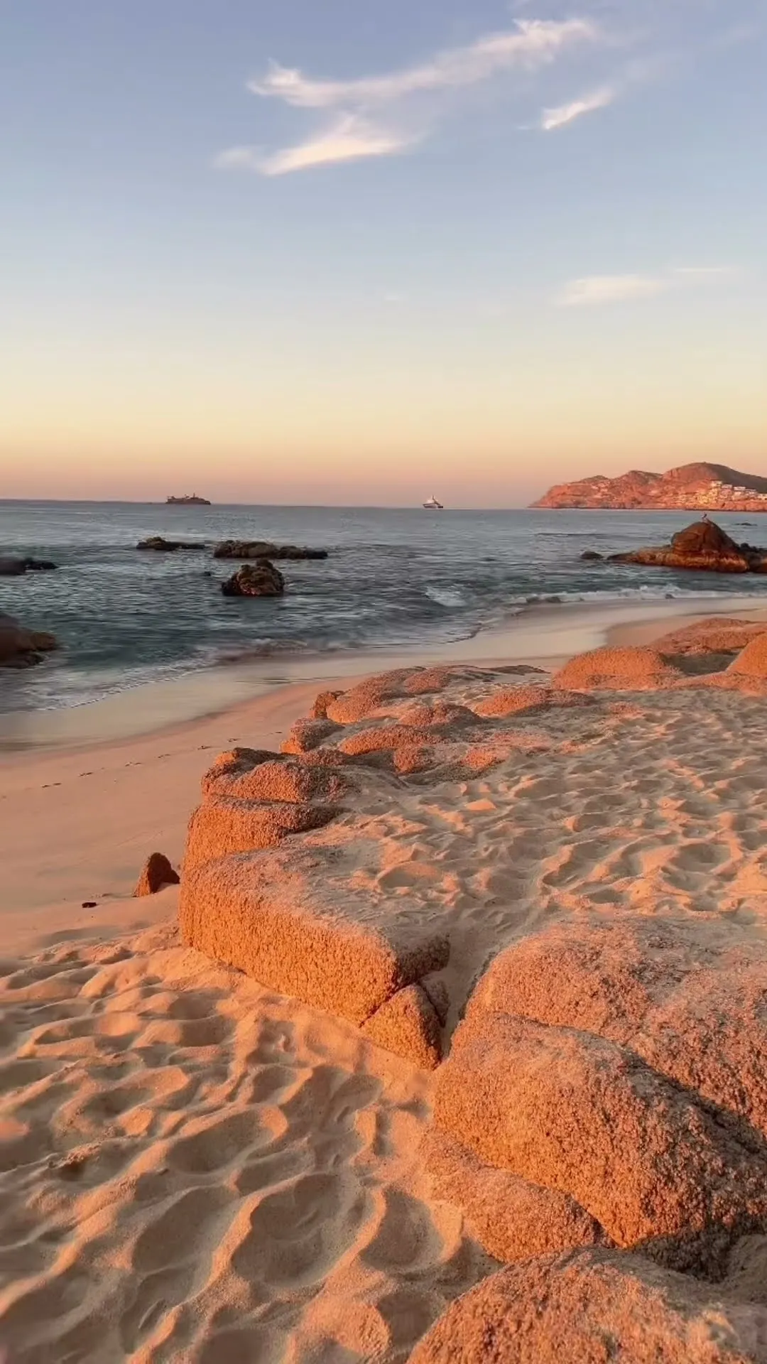 Luz de la hora dorada sobre las rocas y la arena a la orilla del agua en una playa de Los Cabos