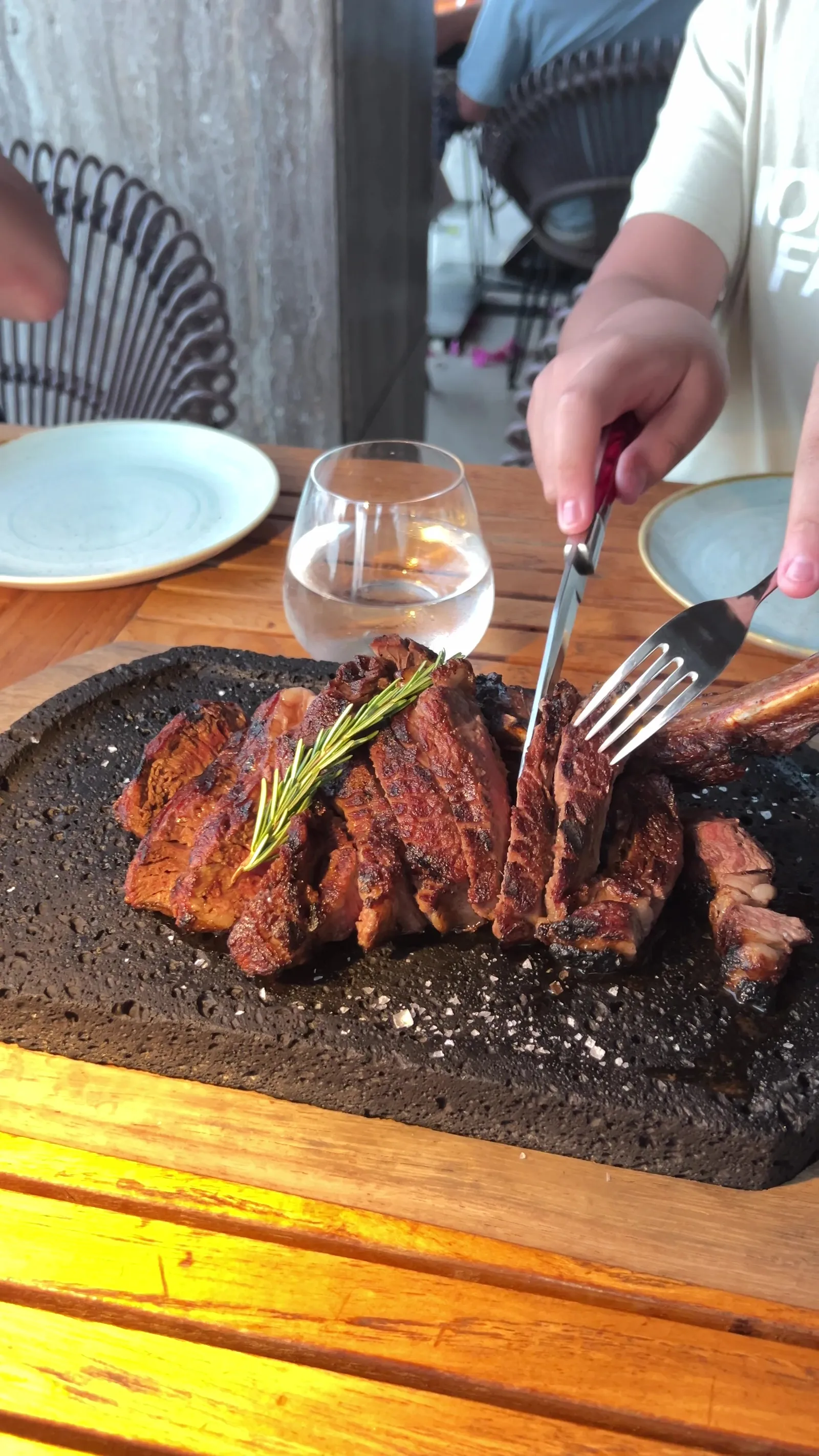 Manos cortando un steak en bandeja de piedra negra