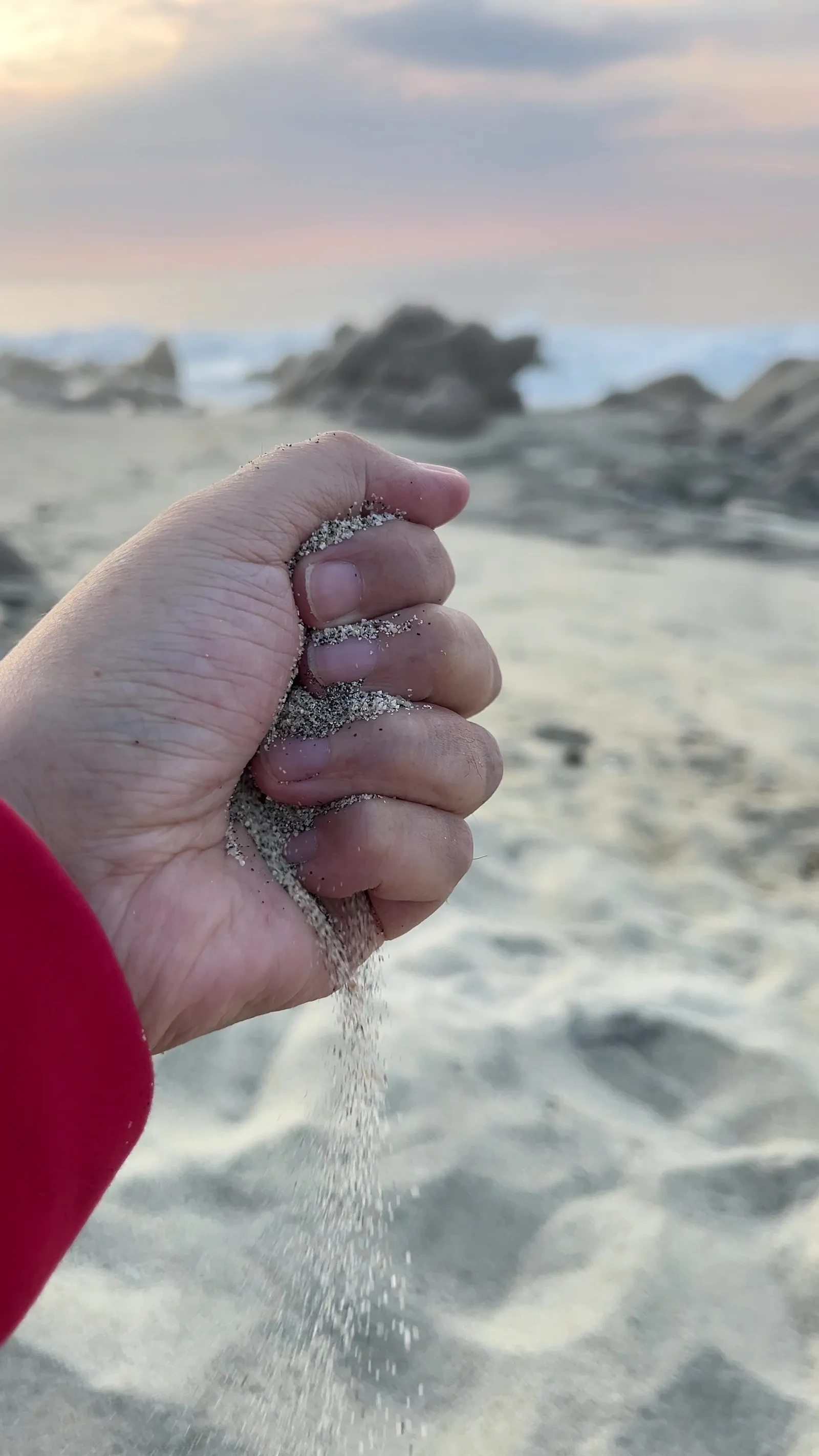 Mano dejando caer arena gruesa con el mar desenfocado detrás