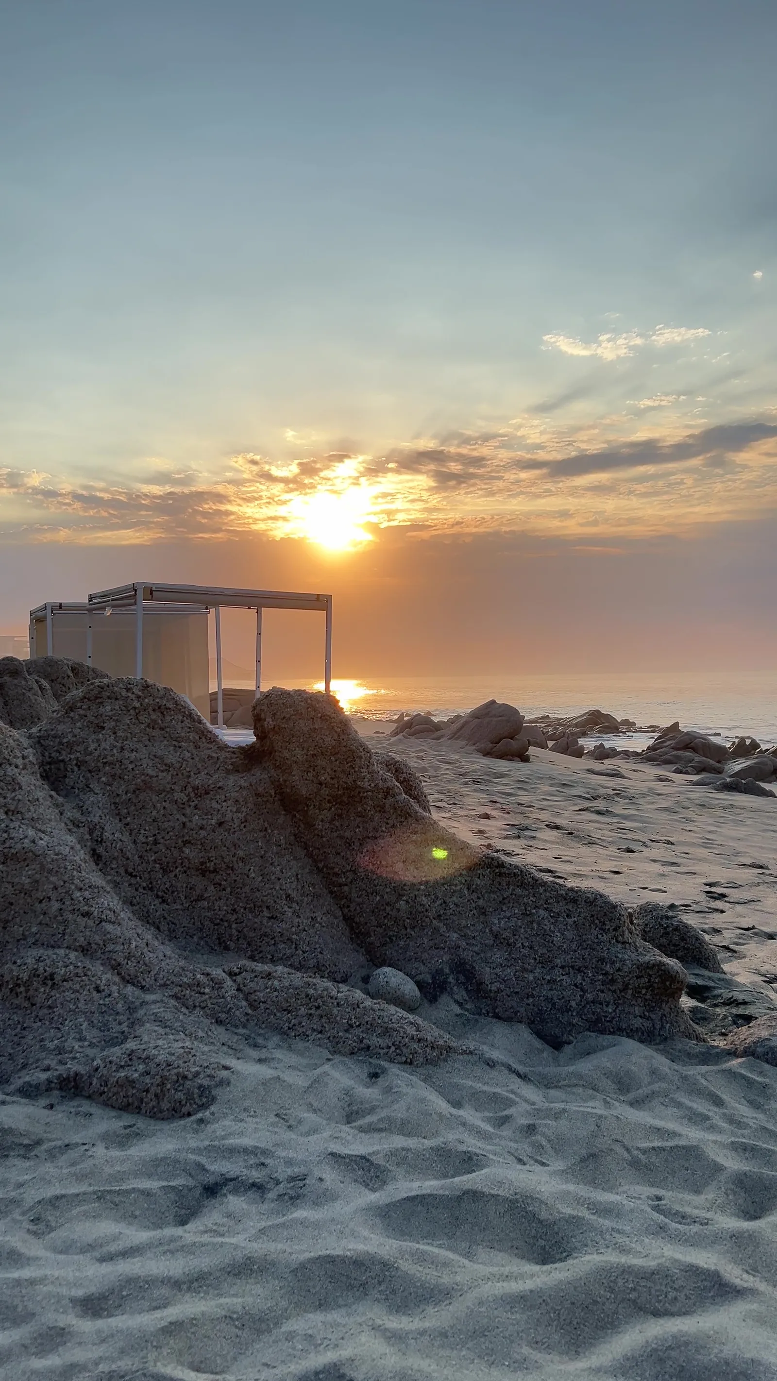 Amanecer dorado sobre rocas y cabañas blancas en Cabo