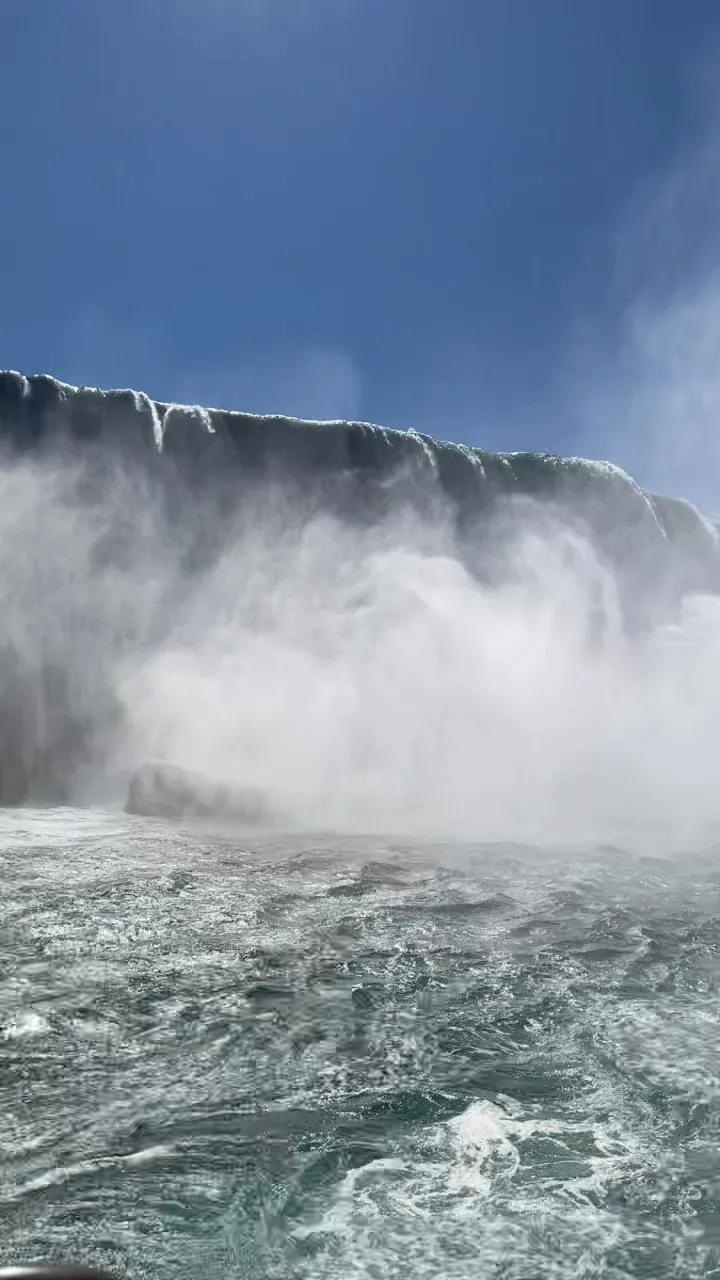 Horseshoe Falls crest pouring into sunlit mist above churning water, seen from the boat