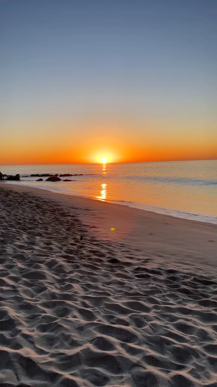 太陽完整升起在 Cabo 海灘上,水面一條金色光路,前景是起伏的沙紋