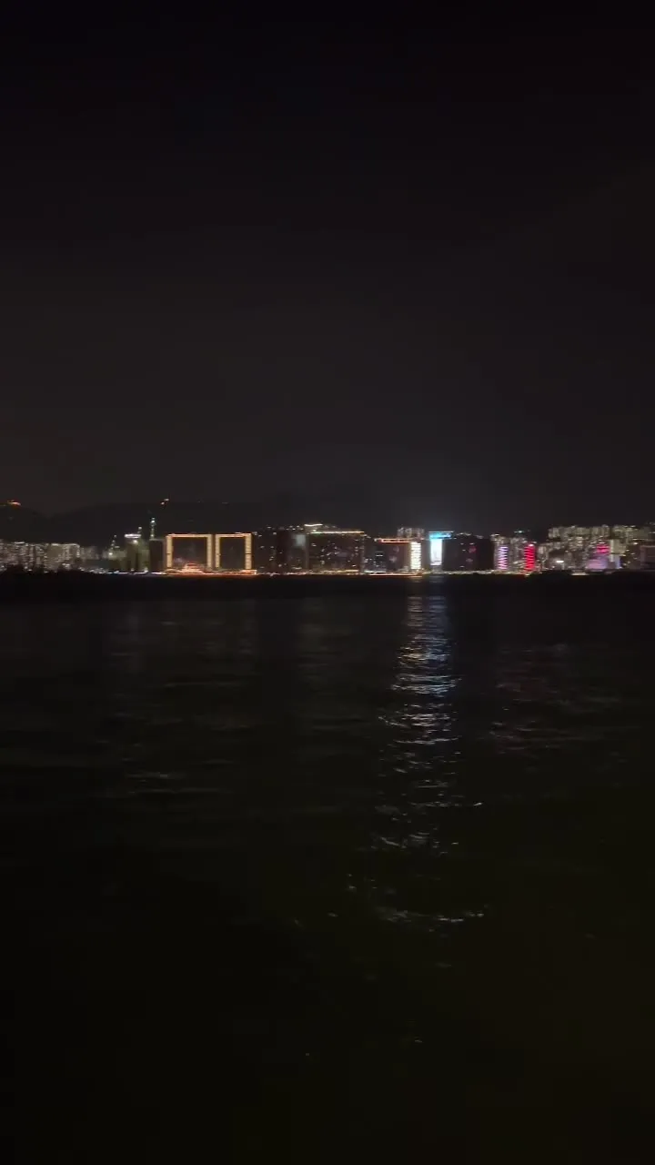 Los edificios y letreros encendidos de la orilla lejana, reflejados en el puerto de noche